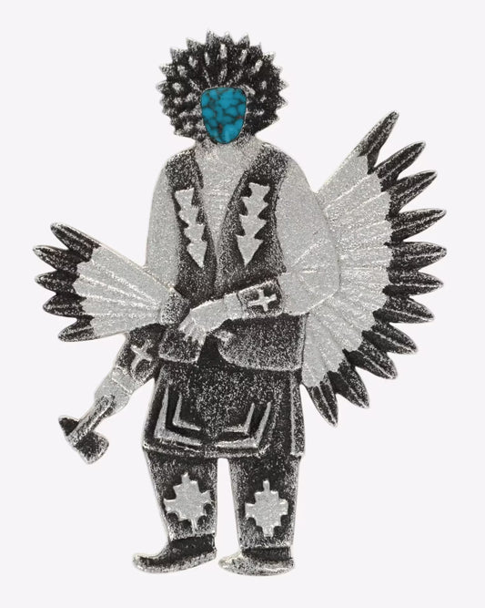 A stylized kachina doll pin or charm with a black and silver glitter finish, featuring a turquoise blue face, black hair, and large wings, shown on a plain white background.