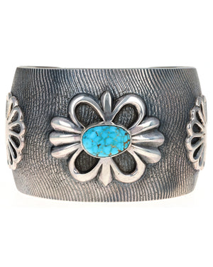 Silver cuff bracelet with floral design and turquoise stone on a white background